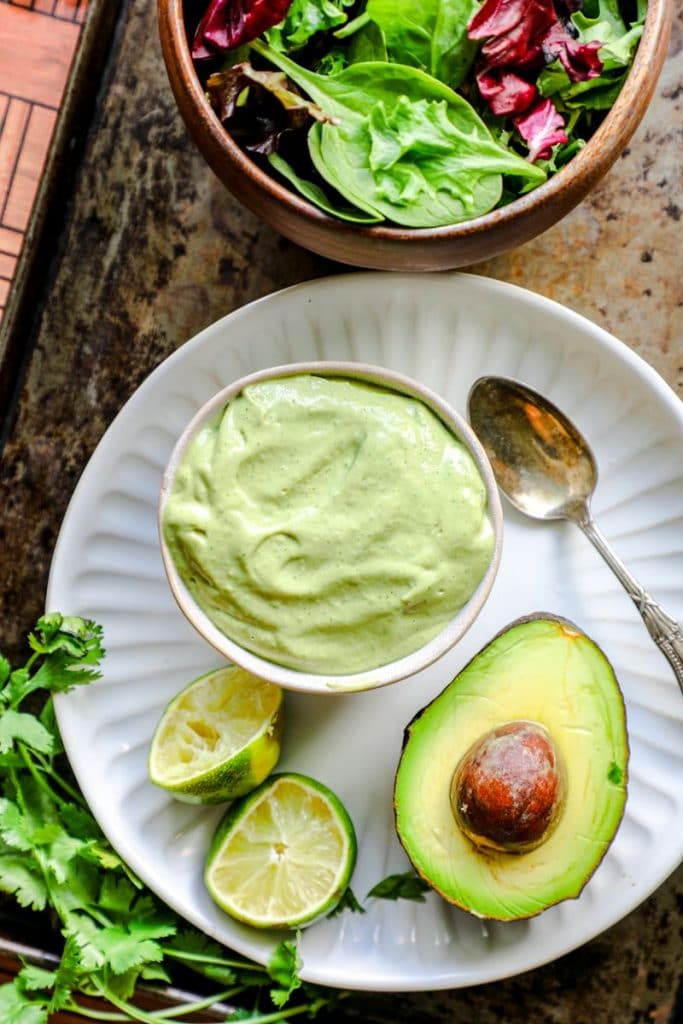 Avocado dressing in a bowl on a tray with an avocado next to it