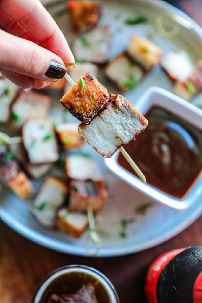 A hand holding pork belly bites on a toothpick