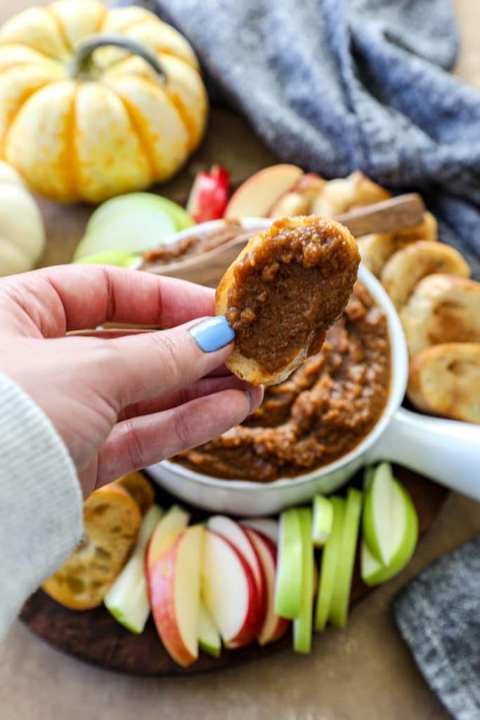 Hand dipping bread into pumpkin butter with pumpkin butter bowl in the background. 