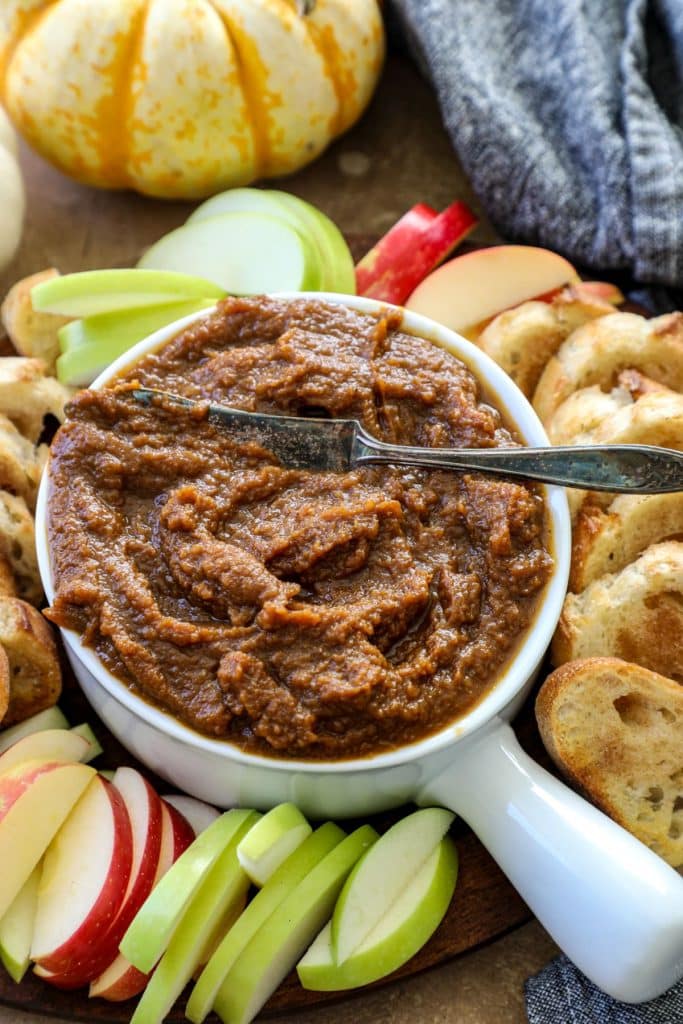 Maple Pumpkin butter in a white bowl surrounded by apples and bread. 