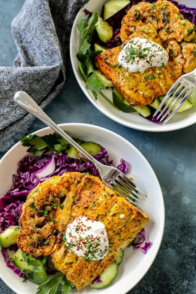 Two white bowls with tandoori salmon over a bed of cabbage and lettuce.