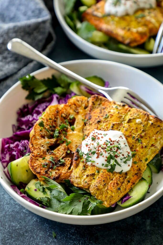 Salmon in a white bowl on a bed of cabbage and lettuce with a silver fork. 