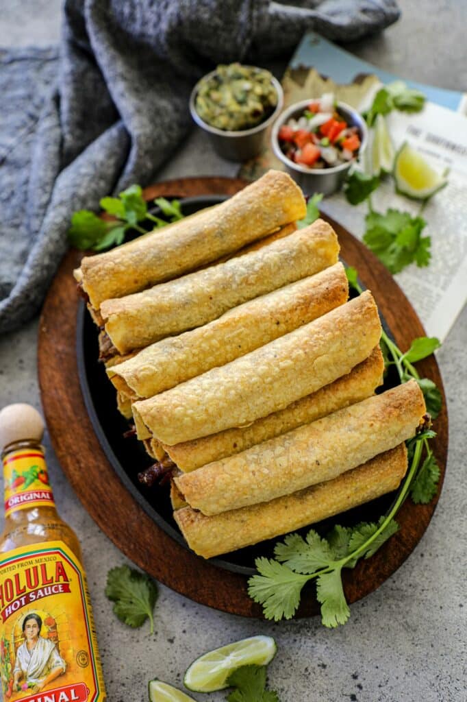 Top view of flautas stacked on top of each other on a black platter next to hot sauce.