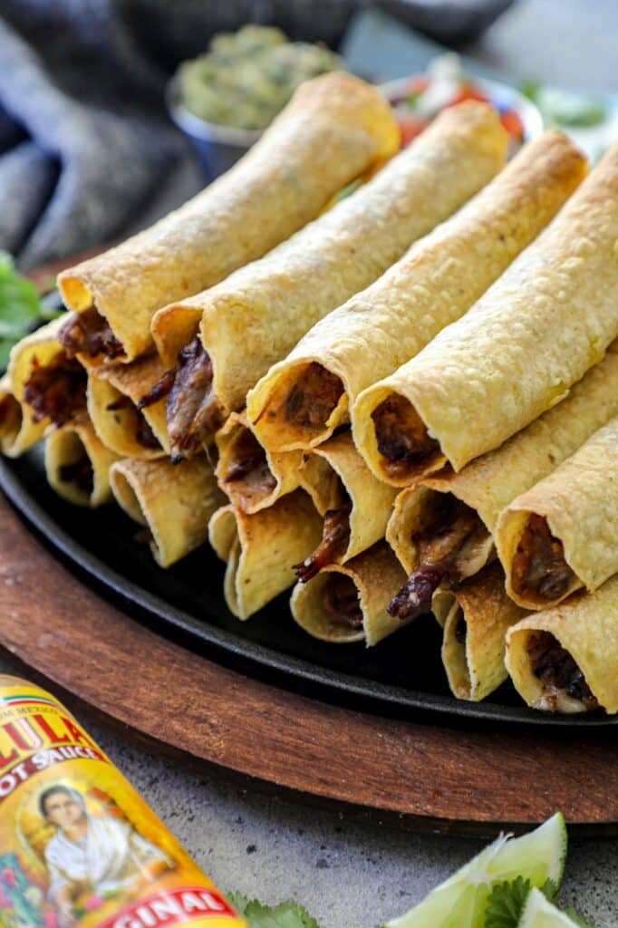 Air Fryer Flautas stacked on top of each other on a black platter.