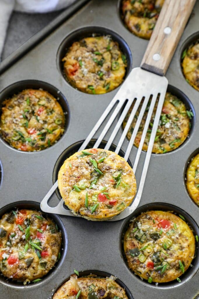 Sausage egg cups in a muffin tin with one egg cup sitting on a spatula.