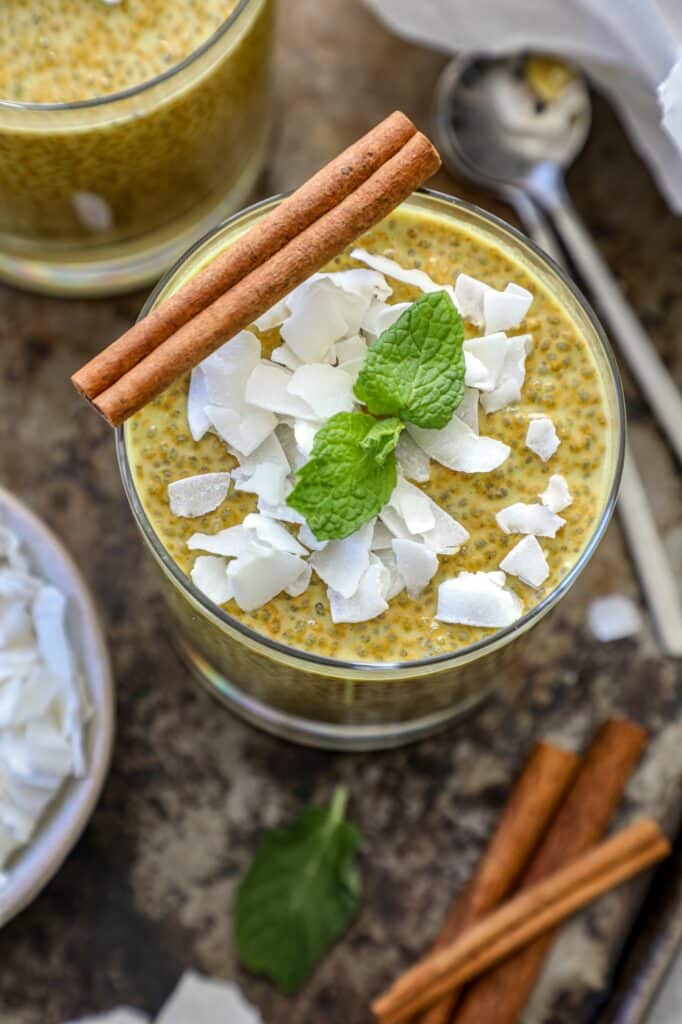 Up close shot of chia pudding topped with coconut flakes, mint, and a cinnamon stick.
