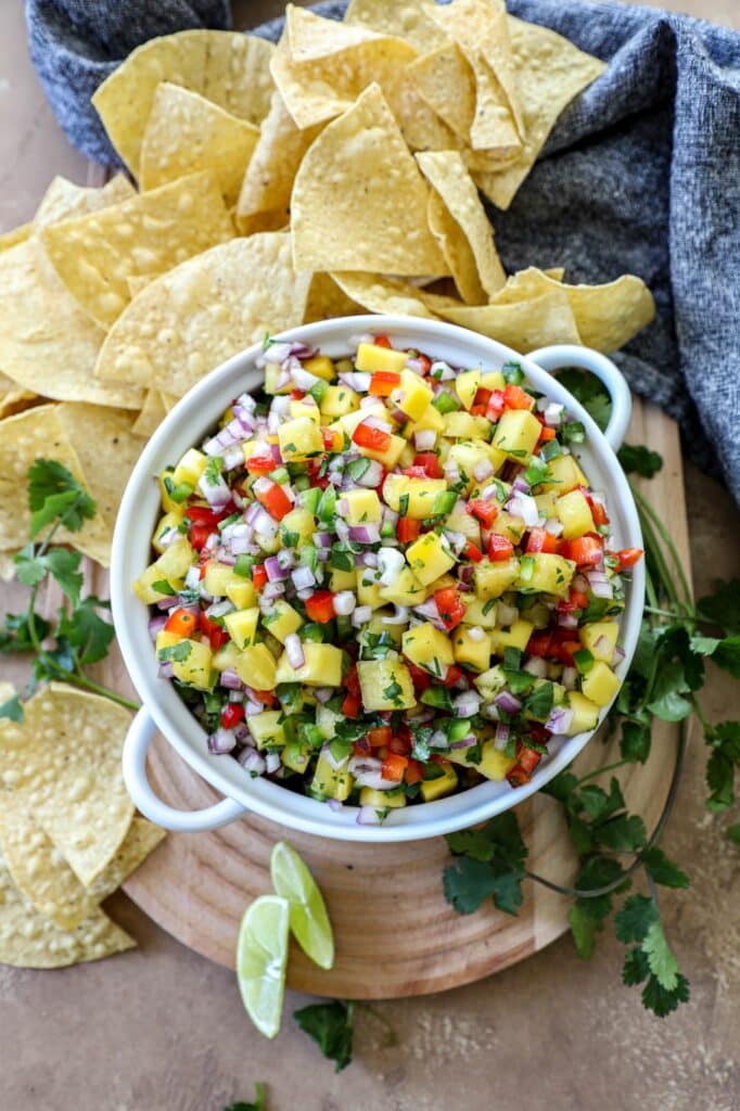 Mango pineapple salsa in a white bowl next to a pile of tortilla chips.