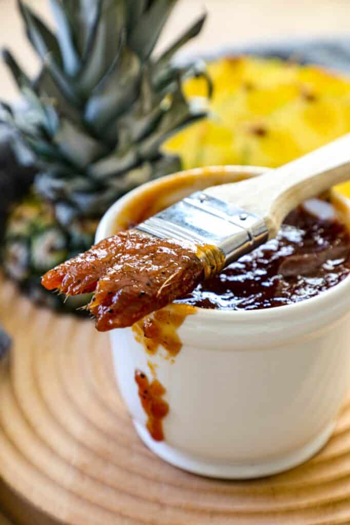 Pineapple BBQ Sauce in a white cup with a brush on top that was dipped in the sauce. 