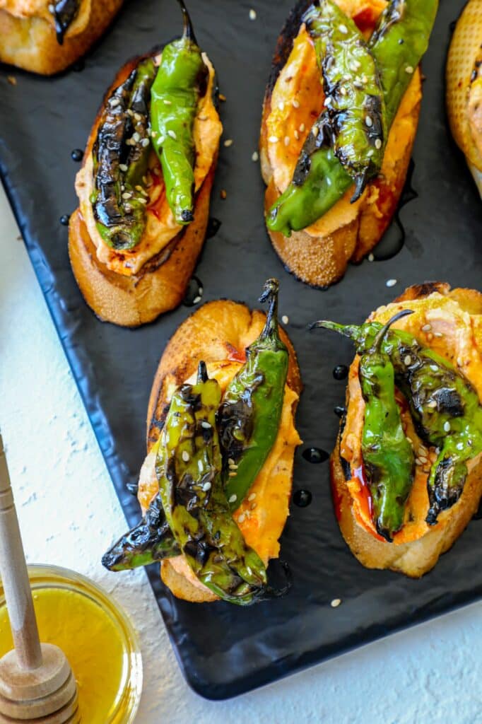 Shishito pepper crostini on a black serving tray. 