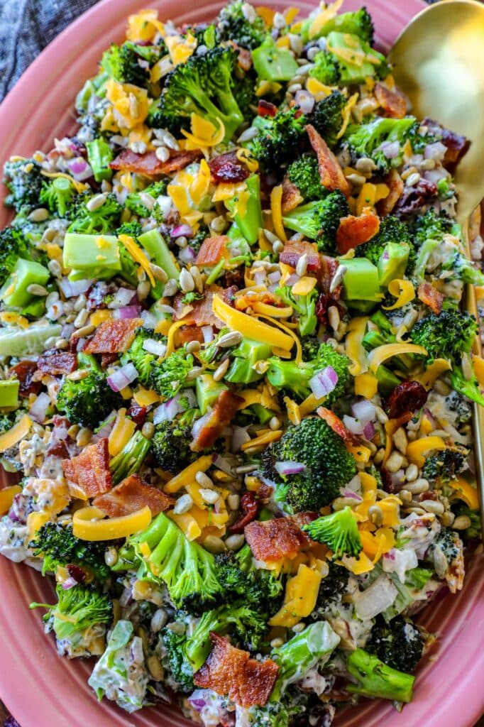 Grilled Broccoli Salad on a pink serving platter with a gold spoon on the side. 