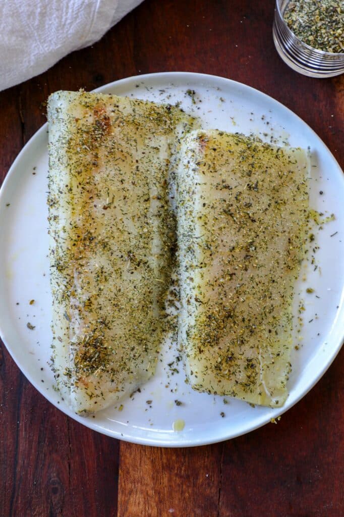 Seasoned cod fillets on a white plate.  