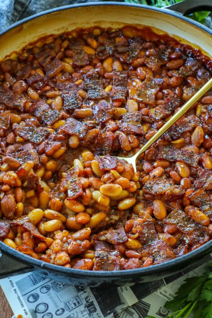 Smoked Baked Beans in a cast iron skillet with a gold spoon. 