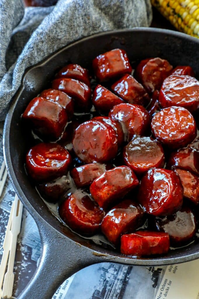 Smoked Sausage pieces in a cast iron skillet, smothered in BBQ sauce. 