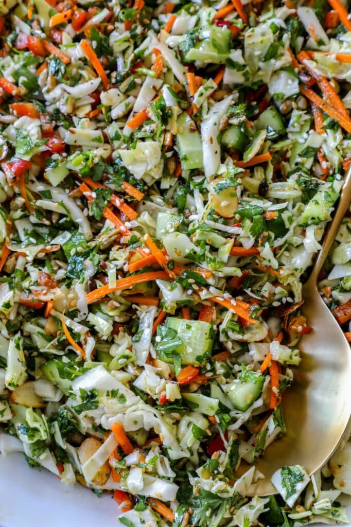 Chopped cabbage salad on a white serving tray with a golden spoon. 