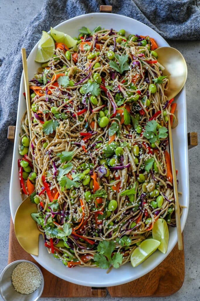 Cold Soba Noodle Salad on a white serving platter with gold serving spoons. 