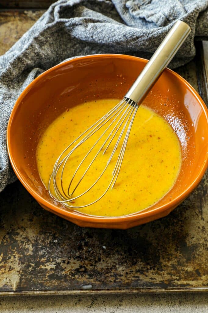 Fire Roasted Hatch Chile Corn Salad dressing in an orange bowl with a whisk.