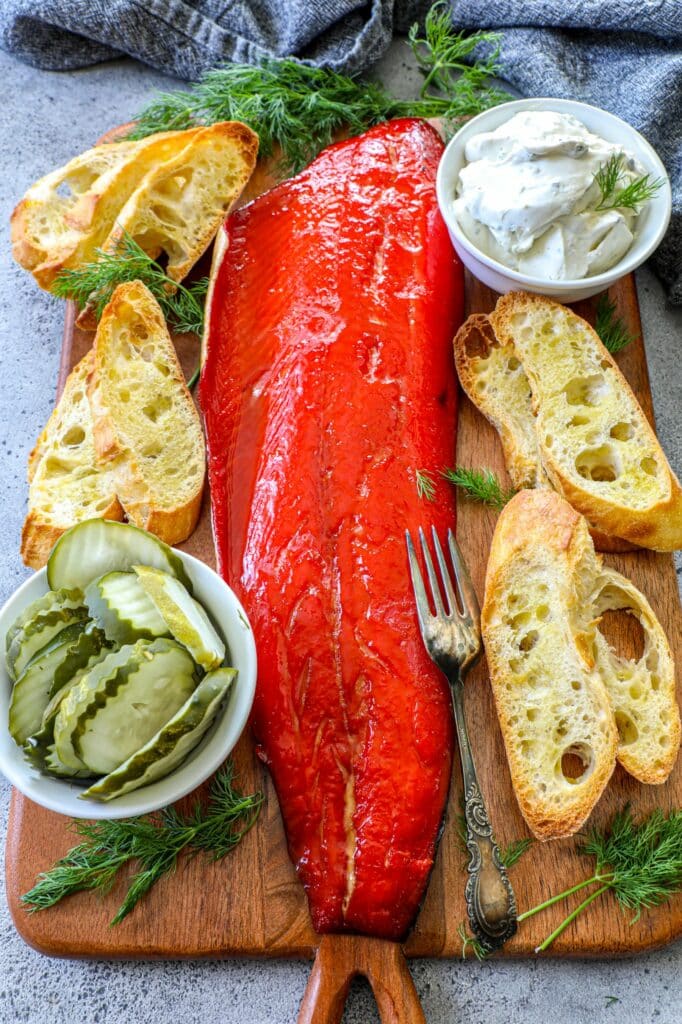 Hot smoked salmon on a cutting board next to bread and pickles. 