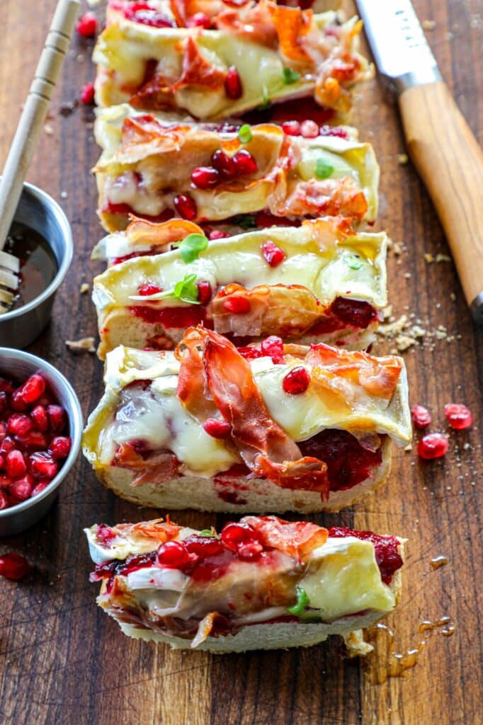 Cranberry, Brie, and Prosciutto Baguette sliced into pieces on a wooden cutting board. 