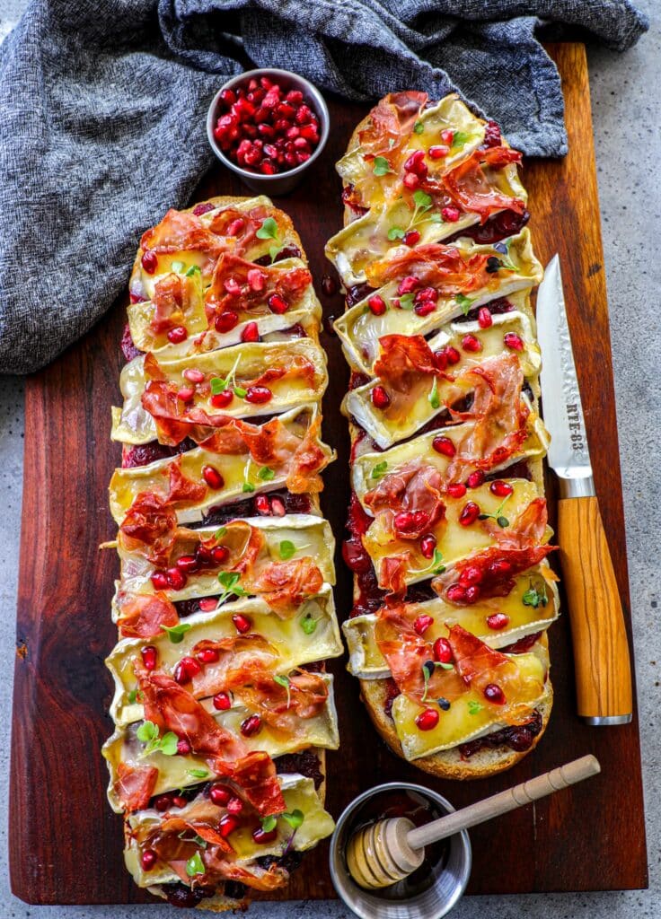 Cranberry, Brie, and Prosciutto Baguette on a wooden cutting board next to a knife.