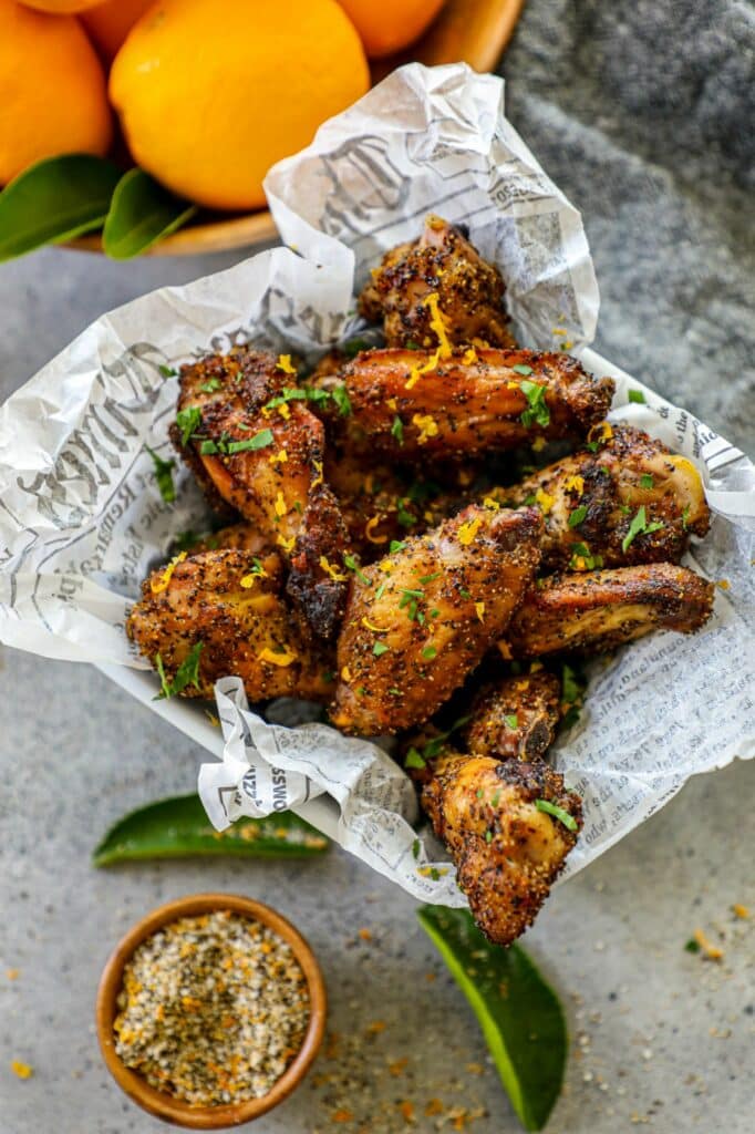 Grilled Lemon Pepper Wings in a basket next to a small bowl of lemon pepper seasoning. 