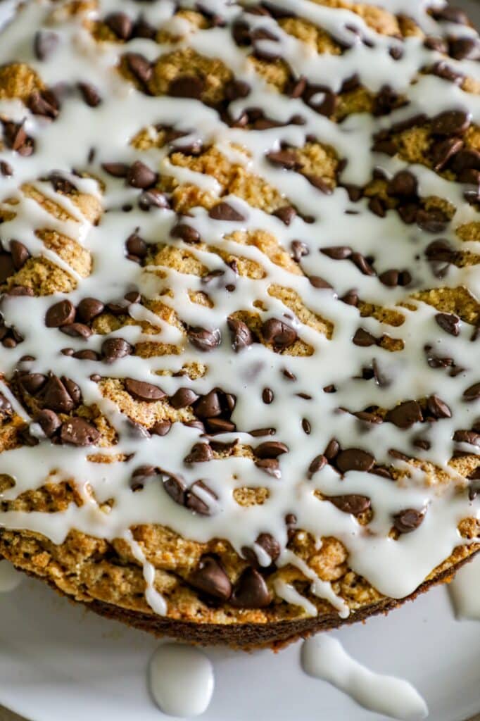 Close up shot of banana coffee cake on a plate topped with chocolate chips and a glaze. 