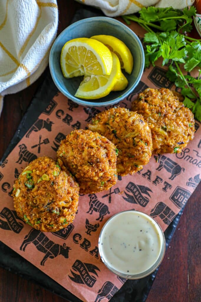 Smoked Crab Cakes Recipe served on a black serving board with a side of lemon wedges. 