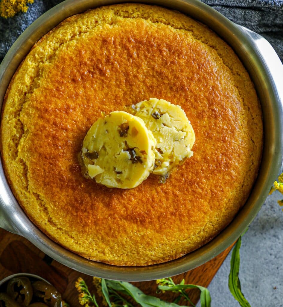 Cornbread in a baking pan with two slices of jalapeño honey butter on top. 